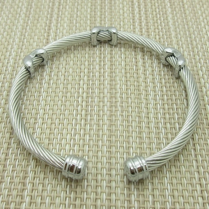 Detail view of a silver twisted cable bangle with smooth metal accents on a textured base