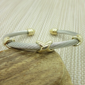 Macro detail of twisted steel rope bracelet featuring gold-tone X-shaped accents on wood