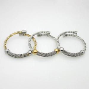 Three-piece stainless steel cable wire bangles in silver and gold tone set on white background