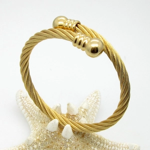 Golden titanium steel twisted cable bangle featuring spherical ends on a starfish prop