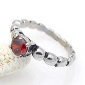 Macro-opname van vintage roestvrijstalen ring met rode zirkoon en een kralenband