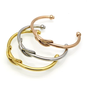 Three polished stainless steel knot cuff bracelets in gold, silver, and rose gold finishes