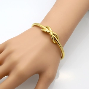 Minimalist gold knot bangle in stainless steel shown on a hand model with a sleek finish