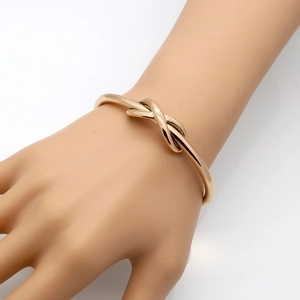 Polished rose gold stainless steel knot bangle bracelet worn on a woman's wrist