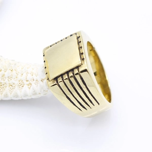 Macro detail of men's square gold signet ring featuring side grooved lines on white starfish
