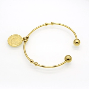 Detailed close-up of 18k gold-plated open bangle featuring a Saint Benedict medal charm