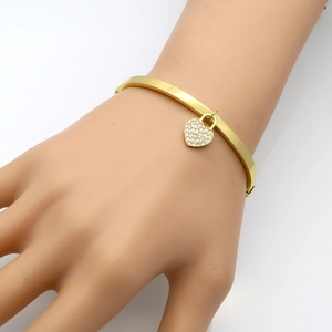 Détail d'un bracelet jonc or rose avec un pendentif en cœur serti de zircons brillants