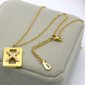 Macro shot of 18KGP engraving on the clasp tail of a dainty gold x-shaped pendant necklace