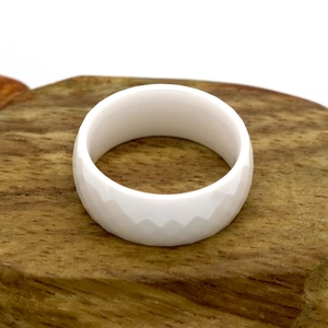 Minimalist white faceted ceramic ring with diamond textures on a natural wood base