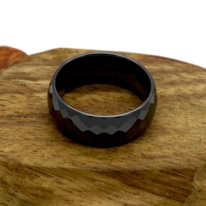 Macro view of a black geometric faceted ceramic ring on a natural wood texture base