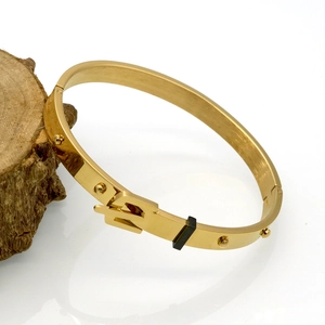 Detail shot of golden belt buckle bracelet with rivets on a rustic wooden stand