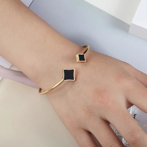 Golden stainless steel cuff bracelet with black geometric diamond star charms on wrist