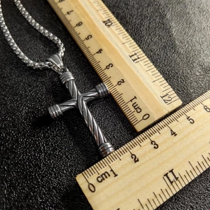 Vintage stainless steel cross necklace with spiral texture displayed on measuring rulers