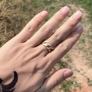 Nahaufnahme eines vergoldeten Panzerketten-Rings, am Finger getragen im Freien