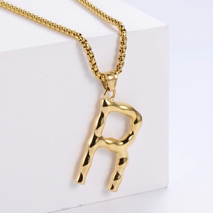 Détail du collier avec pendentif lettre R en relief doré avec texture effet lave
