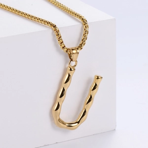 Détail du pendentif lettre U doré avec texture de lave et chaîne box sur support