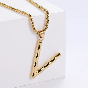 Gros plan du pendentif lettre V dorée à texture bambou sur une chaîne à maillons carrés