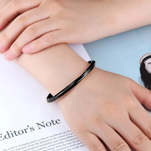 Minimalist black polished Mobius bangle styled on a model wrist over a fashion magazine