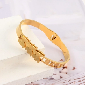 Polished gold stainless steel butterfly bangle with matte finish charms on a display stand
