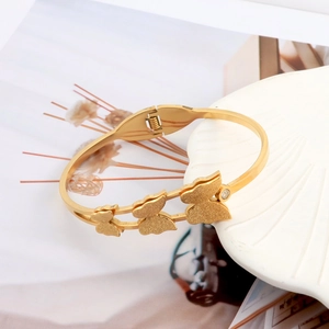 Close-up of golden butterfly bracelet with matte finish and hinge detail on shell backdrop