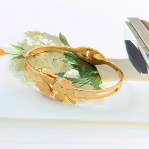 Detail of gold butterfly and four-leaf clover charms on frosted stainless steel bracelet