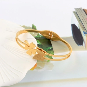 Detail of gold titanium steel double-layer bracelet with butterfly and clover charms