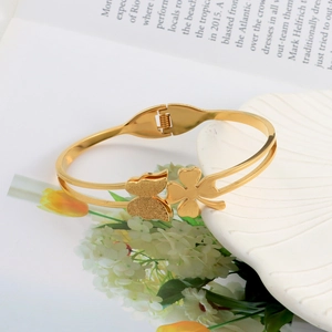 Detail of golden stainless steel butterfly bracelet with clover on a white plate
