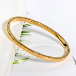Dettaglio di un bracciale rigido minimalista in acciaio dorato con finitura a specchio