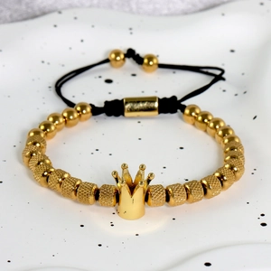 Dettaglio del bracciale con perline a corona d'oro e corda nera su vassoio in ceramica