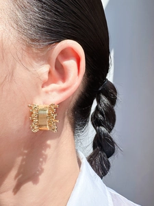 Close-up of golden irregular textured C-shaped earrings worn by a model in bright light