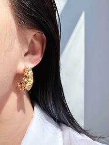 Close-up of golden C-shaped wave earrings with irregular pleated texture on a model