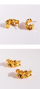 Close-up of golden C-shaped hoop earrings with wavy molten metal texture detail