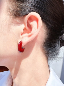 Gros plan de la boucle d'oreille C en émail rouge foncé portée avec base en métal poli