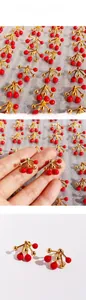 Detailed view of red enamel cherry-shaped stud earrings with gold metallic finish