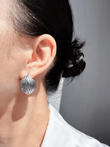 Détail d'une boucle d'oreille argentée avec texture coquillage et rayures verticales