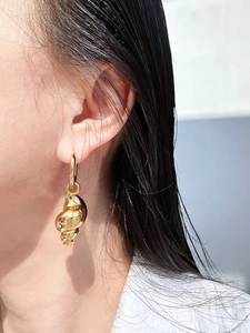 Macro shot of gold spiral conch shell pendant earrings on ear with high-gloss finish