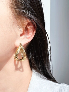 Gros plan détaillé de boucles d'oreilles dorées goutte à texture lave sur un mannequin