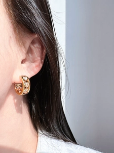 Detail of C-shaped gold-plated earring with hollow design and three heart zircons on ear