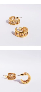 Detail of C-shaped gold earrings featuring hollow heart patterns and cubic zirconia stones