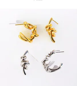 Detailed view of asymmetric twisted knot C-shaped earrings in gold and silver finish