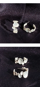 Detail view of silver C-shaped earrings with unique hammered metal disc textures