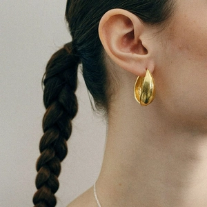 Gros plan d'un modèle portant des boucles d'oreilles goutte d'or épaisses au fini brossé