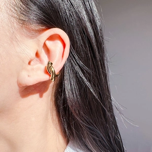 Close-up of a minimalist golden twisted ear cuff showing its sleek curved design on the ear