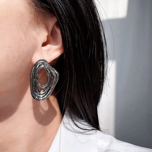 Close-up of a model wearing large silver irregular spiral oval earrings with polished finish