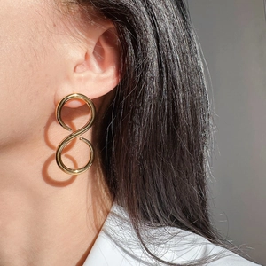 Detail of oversized gold twisted figure-eight stud earrings with a glossy metal finish