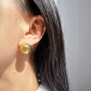 Macro view of gold woven ball earrings showing intricate metallic texture on ear