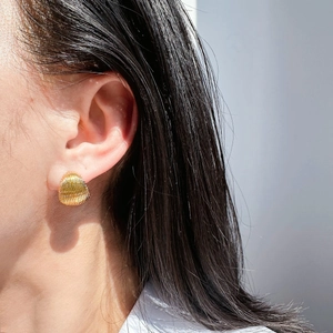 Macro view of gold shell textured stud earring worn on ear showing fine curved lines