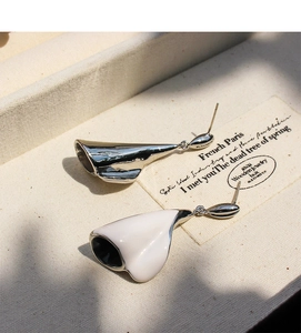 Macro detail of elegant white enamel and silver calla lily leaf earrings on vintage card