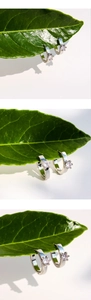 Detail of silver hoop earrings with six-prong set cubic zirconia on green leaves