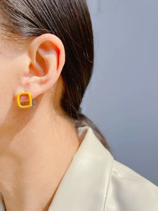 Close-up of model wearing square orange enamel hoop earrings with silver metal base